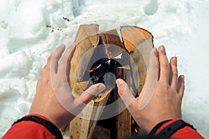 Close-up photo - tourist warms his hands near the fire in the wi