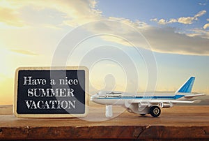 Close up photo of toy airplane next to blackboard with text: HAVE A NICE SUMMER VACATION, against sky with clouds