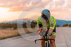 Close up photo of triathlete riding his bicycle during sunset, preparing for a marathon. The warm colors of the sky