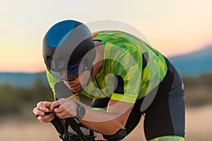 Close up photo of triathlete riding his bicycle during sunset, preparing for a marathon. The warm colors of the sky