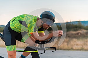 Close up photo of triathlete riding his bicycle during sunset, preparing for a marathon. The warm colors of the sky