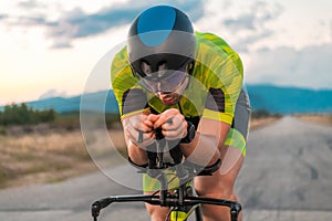 Close up photo of triathlete riding his bicycle during sunset, preparing for a marathon. The warm colors of the sky