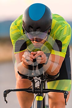 Close up photo of triathlete riding his bicycle during sunset, preparing for a marathon. The warm colors of the sky