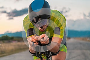 Close up photo of triathlete riding his bicycle during sunset, preparing for a marathon. The warm colors of the sky