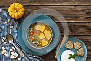 Close-up photo of two plates with fresh homemade pumpkin cream soup with seeds and heart shape toasts