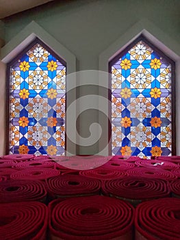 close up photo of two windows with decorative glass above the red mosque carpet
