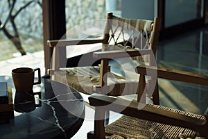 Close up photo of two wooden chairs with woven rope seats at a black marble table, with coffee and a book on the table