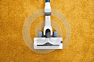 Close-up photo of vacuum cleaner applied on yellow carpet at home removing dust