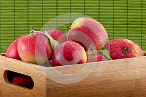 Close-up photo of wet apples in a bamboo crate on green background