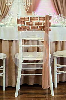 Photo of white chairs decorated with brown textil in a banquet hall in white and brown colors decorated for the event photo