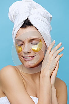 Close-up photo, a woman with clean skin on a blue background with a towel on her head and body takes care of her face