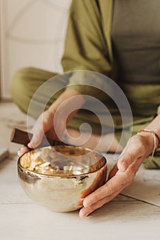 Close up photo of woman hands holding playing on Tibetan singing bowl while sitting on yoga mat. Vintage tonned. Soft focus,