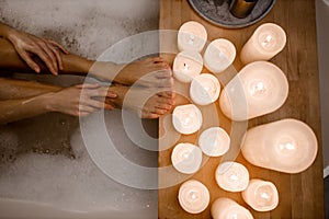 Close up photo of woman& x27;s body in spa bathtub with foam and wooden table vase of plant candle. Modern spa center.