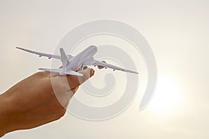 Close up photo of woman`s hand holding toy airplane against sunny sky with clouds. Concepts of travel, transportation, dreaming