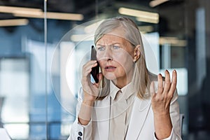 Close-up photo. Worried and upset senior business woman talking on the phone in the office and spreading her hands