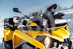 Close-up photo of yellow ATV 4wd quad bike stand in heavy snow with deep wheel track.