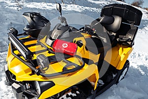 Close-up photo of yellow ATV 4wd quad bike stand in heavy snow with deep wheel track. First aid kit.