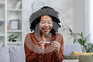 Close-up photo. A young African American woman is happy with a positive pregnancy result. Sitting at home on the sofa
