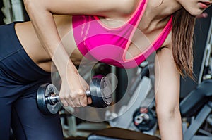 Close-up photo of Young beautiful woman doing exercises lifting dumbbell in gym. Girl is enjoying with her training process