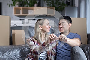 Close-up photo of a young family in a new apartment holding the keys to the house, a multiracial couple sitting in the living room