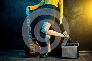 Close-up photo of young hipster woman legs and red guitar in neon lights. Rock musician is playing electrical guitar