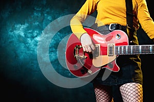 Close-up photo of young hipster woman legs and red guitar in neon lights. Rock musician is playing electrical guitar