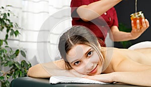 Close up photo of a young pretty blond woman lying on a massage table looking at the camera whilr masseur preparing