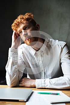 Close-up photo of young thinking curly readhead man, sitting on