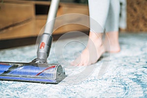 Close up photo of young woman using vacuum cleaner cleaning carpet floor at home