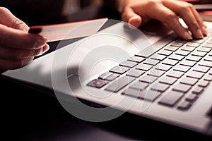 Close up photography of female hands holding a plastic credit card and using laptop. Online shopping concept