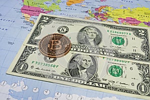 Close up physical bitcoin coin with US dollars and world map.