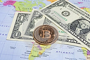 Close up physical bitcoin coin with US dollars and world map.