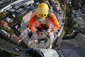 Close up pic of male rope access jobs worker wearing yellow hard hat, long sleeve shirt, safety harness, working at height