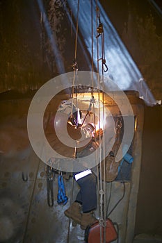 Close up pic of rope access welder wearing safety equipment abseiling hanging on harness as fall arrest position welding repairs