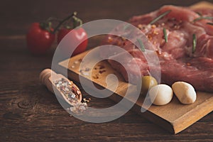 Close-up on pickled pork steaks and next to a wooden spoon, stingy, scoop with spices, all this lies on a wooden background