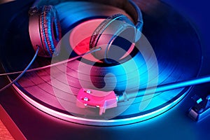 Close-up of a pickup head, black headphones on a vinyl record, colored lights, analogue retro music concept, audio experience,