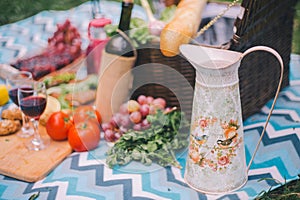 Close-up picnic in nature. Jug and food - greens, tomatoes, grapes, wine, baguette