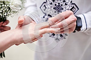 Close up picture of bride and groom`s hands putting on a wedding ring at official marriage ceremony. Bride and groom are getting