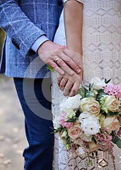Close-up picture of bride`s and groom`s hands, holding each other and beautiful white and pink flower rose bouquet. Close-up