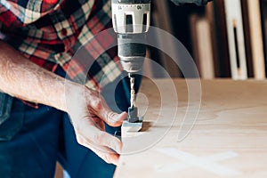 Man holding a drill on a wood plank