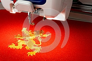 Close up picture of embroidery machine and gold lion logo on the red fabric