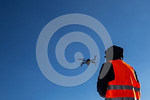 Close up picture of flaying quadrocopter dron and pilot siluette in sunset light and blue sky background, Man flying a drone in