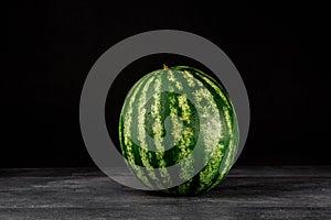 Close-up picture of a fresh and perfect round striped watermelon on a black background. Healthful and organic food. Copy space.