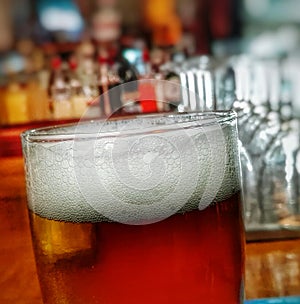 Close up picture of glass of beer with white foam head and blurred backround