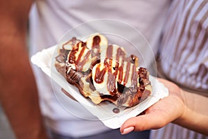 Close-up picture of hand, holding belgian waffle covered with chocolate and caramel. Romantic couple on a date eating desert.