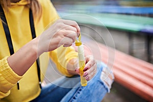 Close-up picture of hands with soap bubbles in process of making them. Young blond woman, wearing yellow hoody, blue jeans and