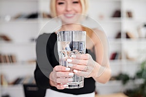 Close-up picture of huge glass of water in hands of young blond woman, standing in office room. Manager at workplace. Work process
