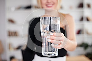 Close-up picture of huge glass of water in hands of young blond woman, standing in office room. Manager at workplace. Work process