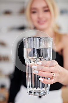 Close-up picture of huge glass of water in hands of young blond woman, standing in office room. Manager at workplace. Work process