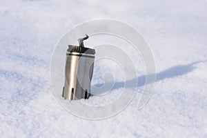 Close up picture of thermos with hot coffee in snow of winter.